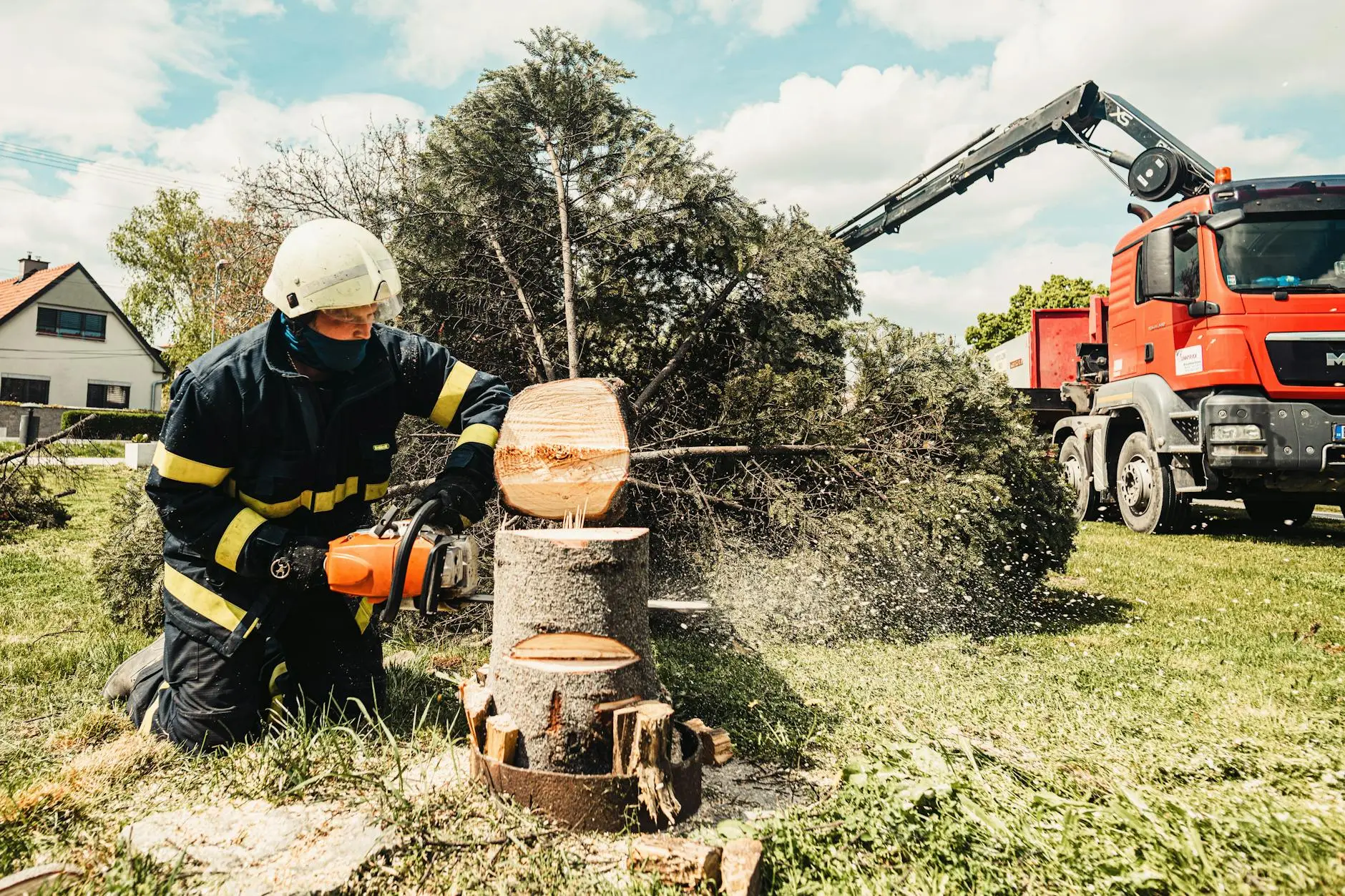 An experienced tree worker wearing full safety gear operating a chainsaw to carefully dismantle a tree branch.